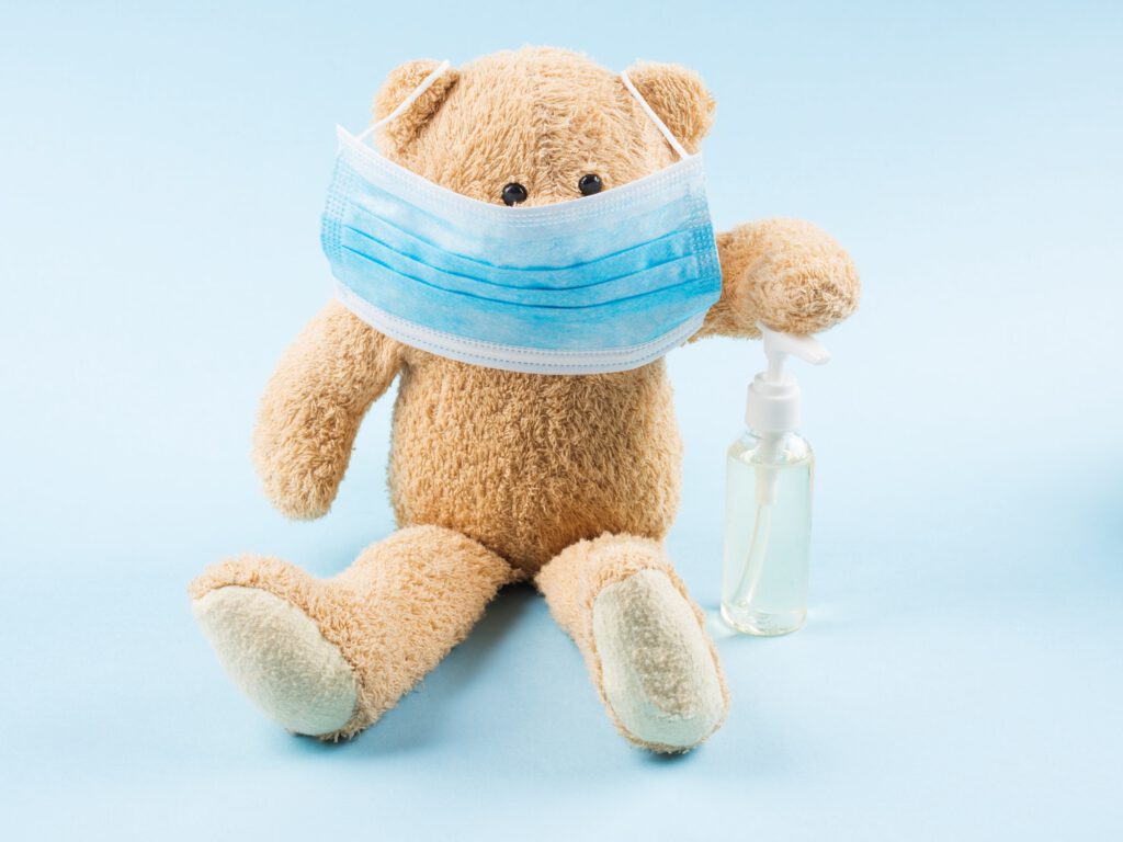 Teddy bear wearing medical face mask and holding sanitiser gel for hands. Instruction for kids